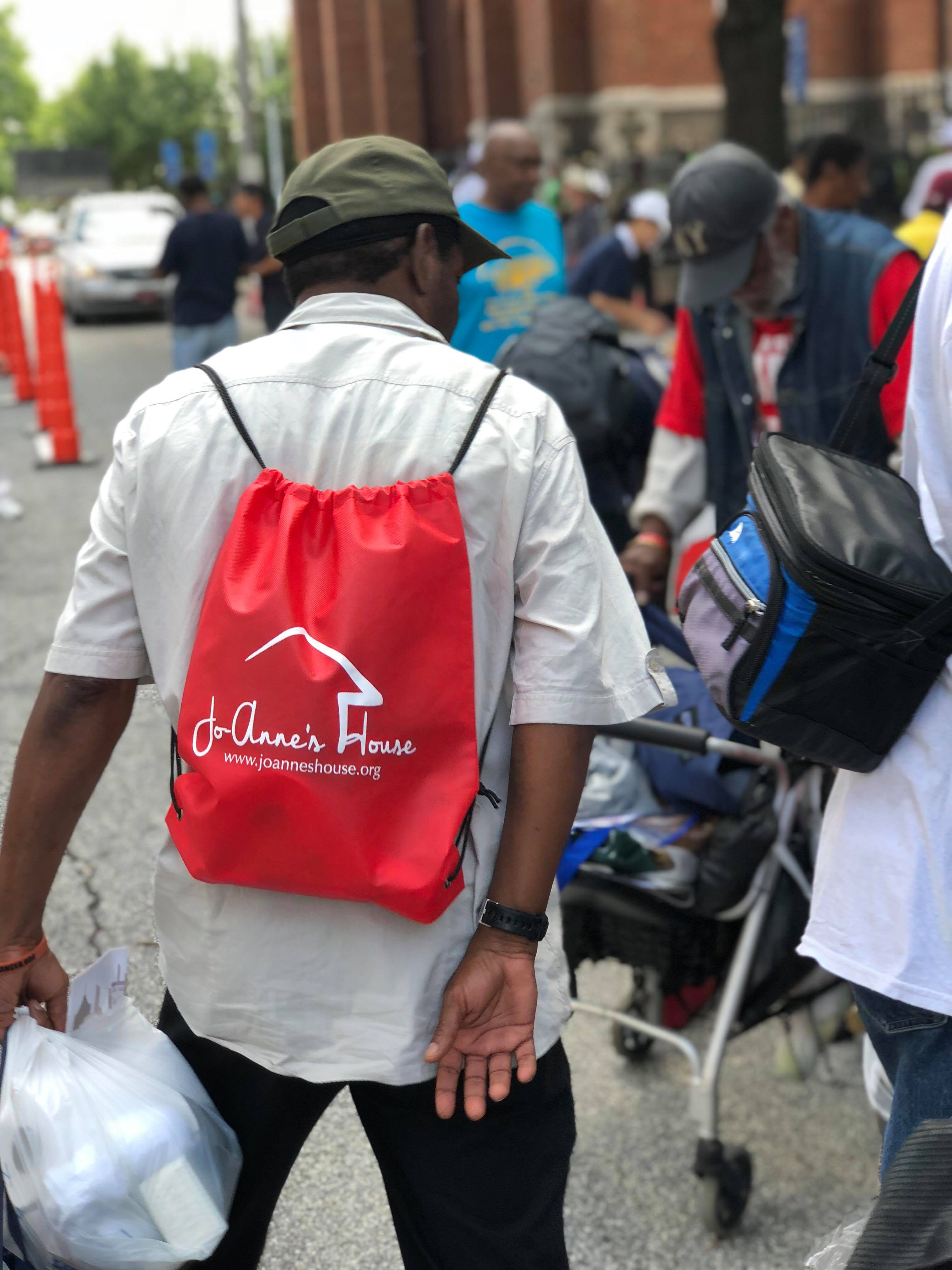 A man wearing a red Jo-Anne's House drawstring bag walking through the outreach crowd
