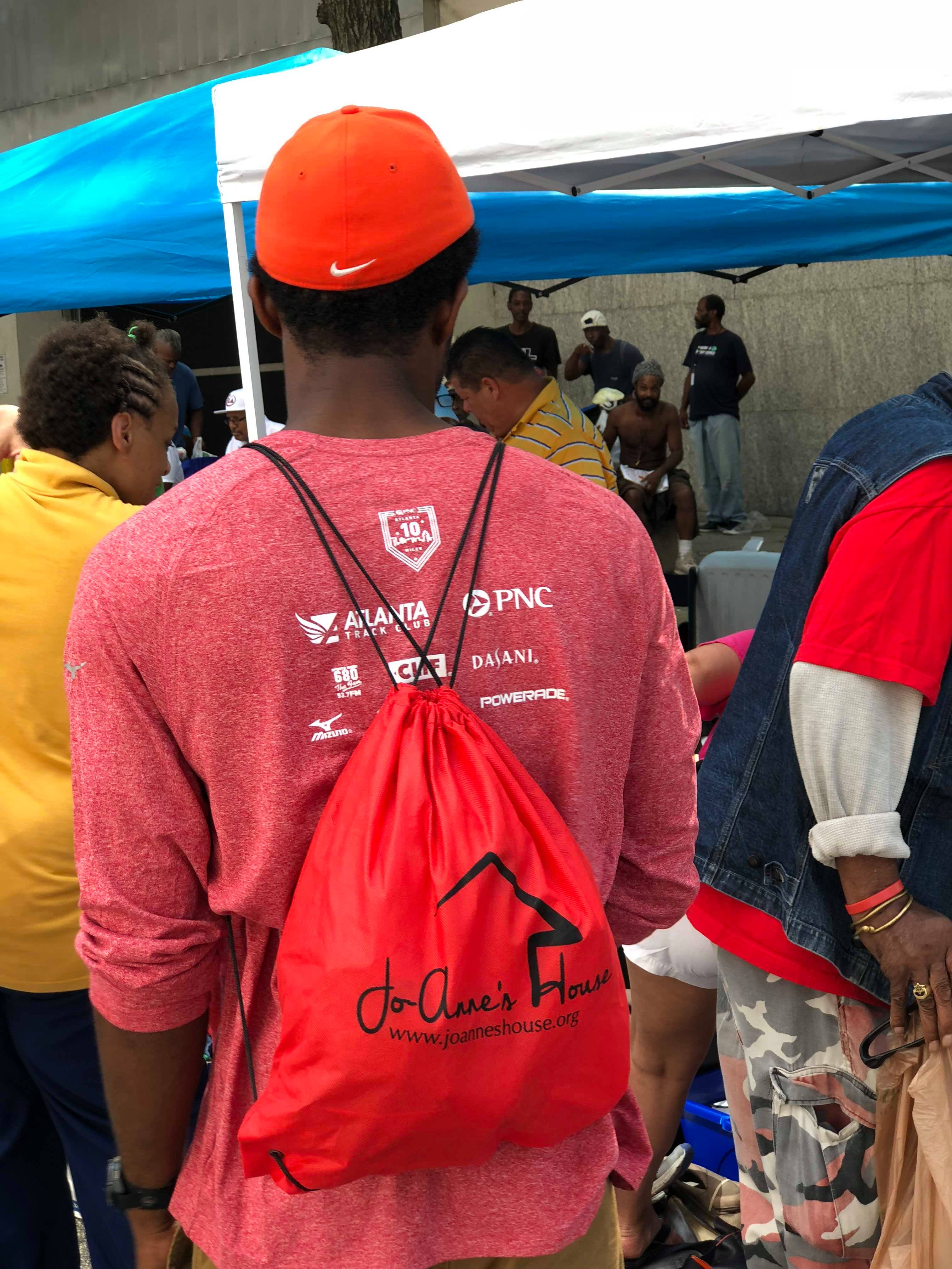 A man in an orange cap carrying a red Jo-Anne's House bag under the event tents