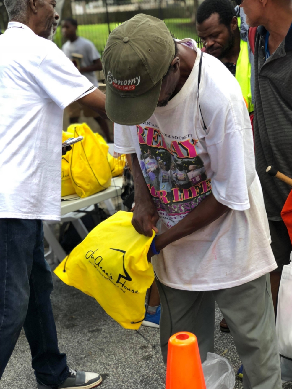 A man receiving a yellow Jo-Anne's House care bag from a volunteer with a clipboard