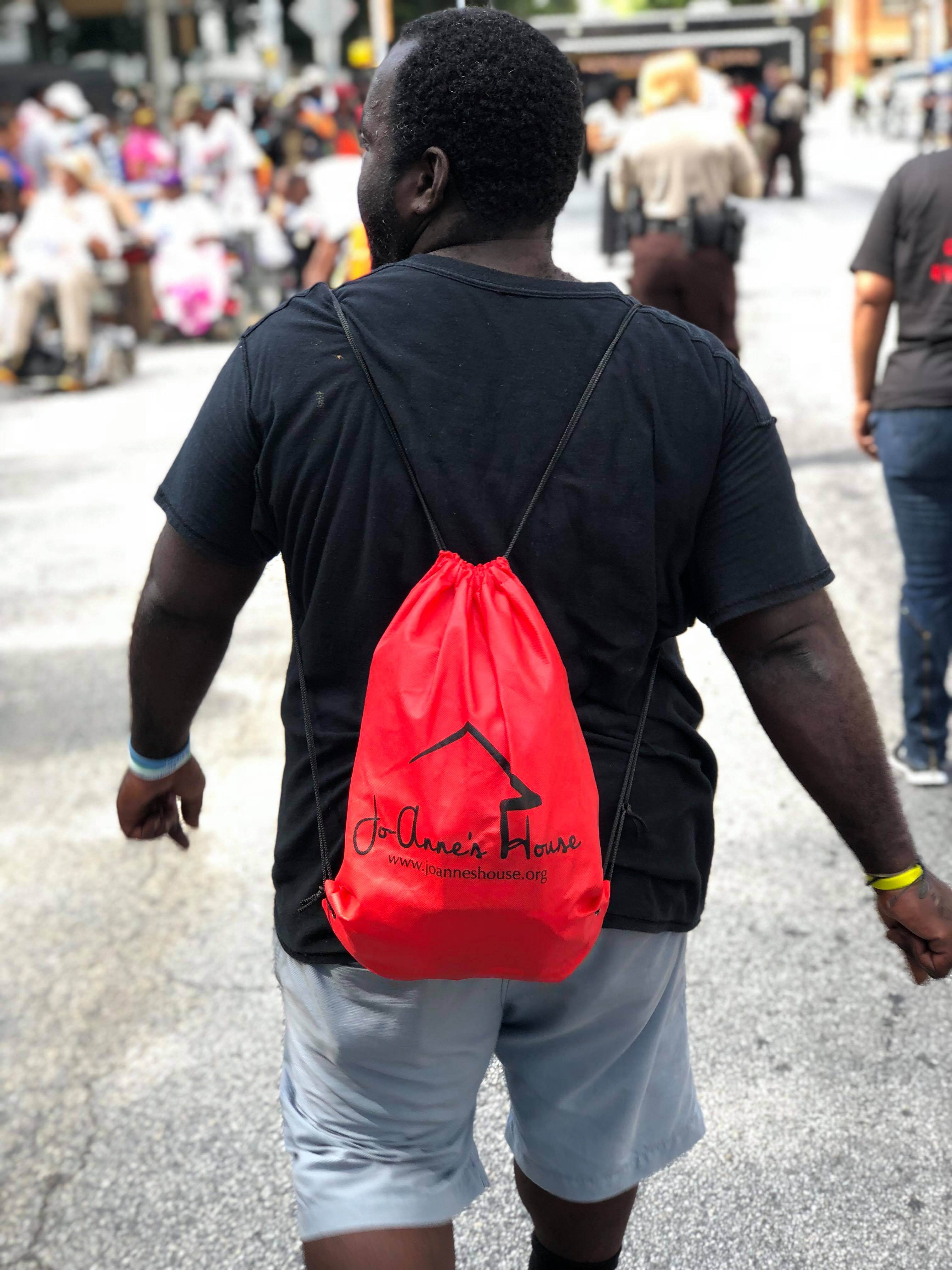 A man wearing a red Jo-Anne's House drawstring backpack walking down the street