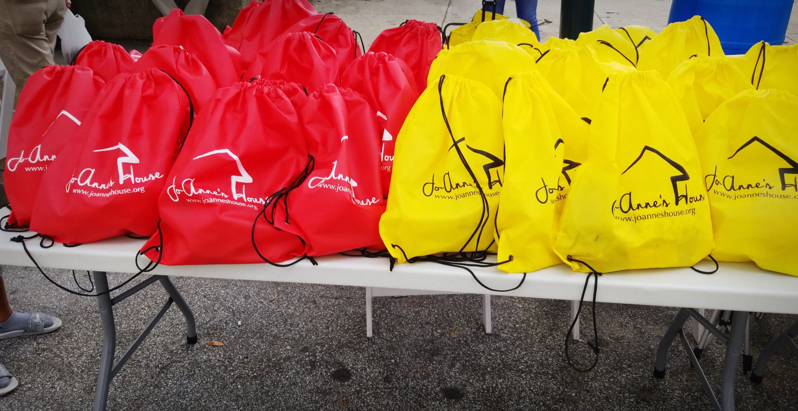 A table covered with rows of red and yellow Jo-Anne's House care bags