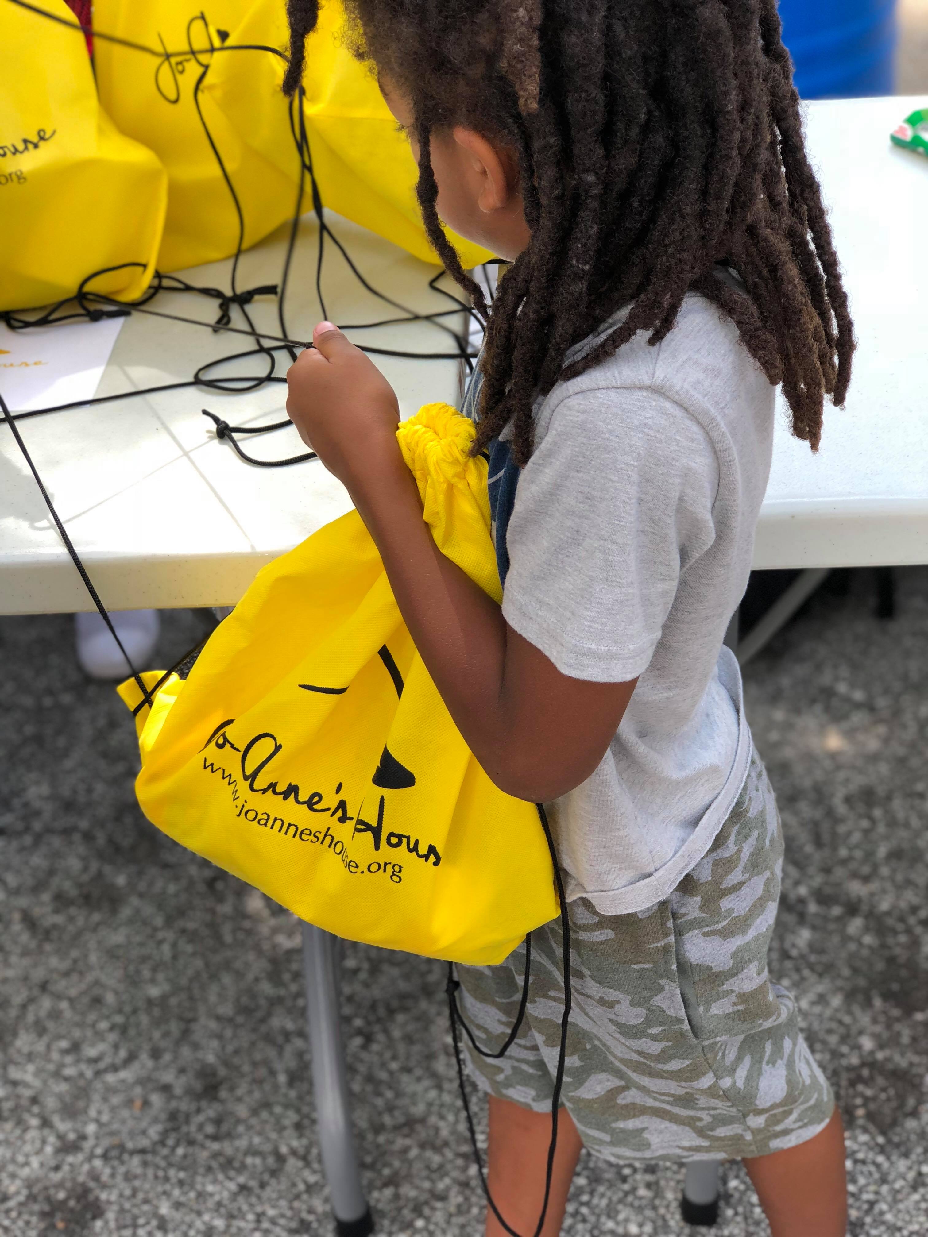 A child cinching a yellow Jo-Anne's House care bag at the supply table