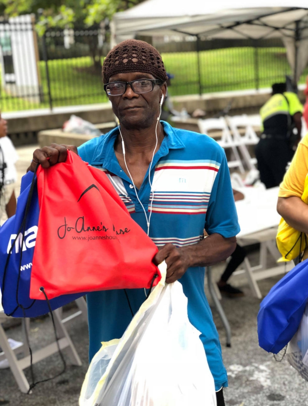 A man holding up a red Jo-Anne's House care bag and a bag of supplies