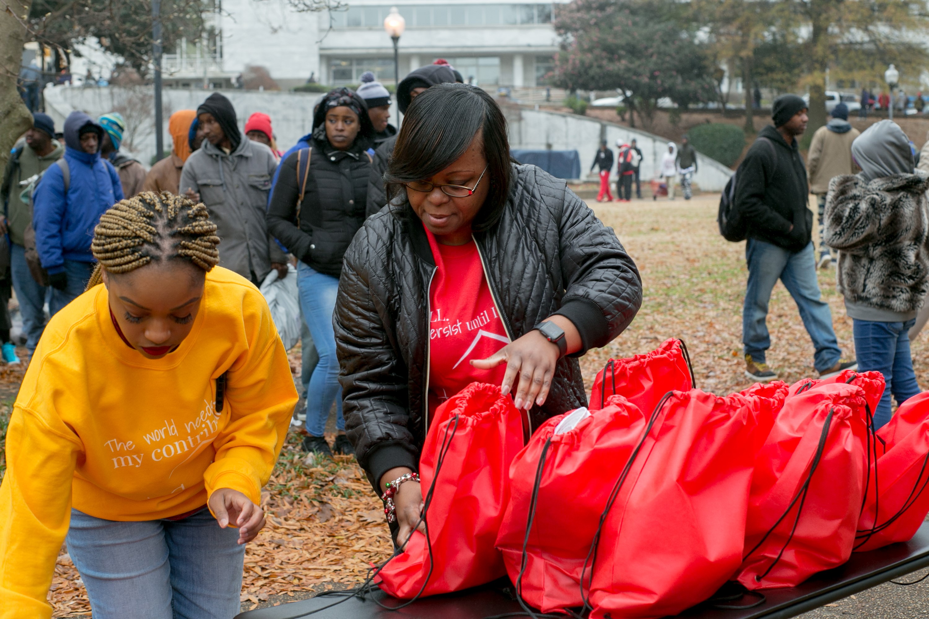 Two volunteers sorting rows of red Jo-Anne's House care bags on a table as recipients wait