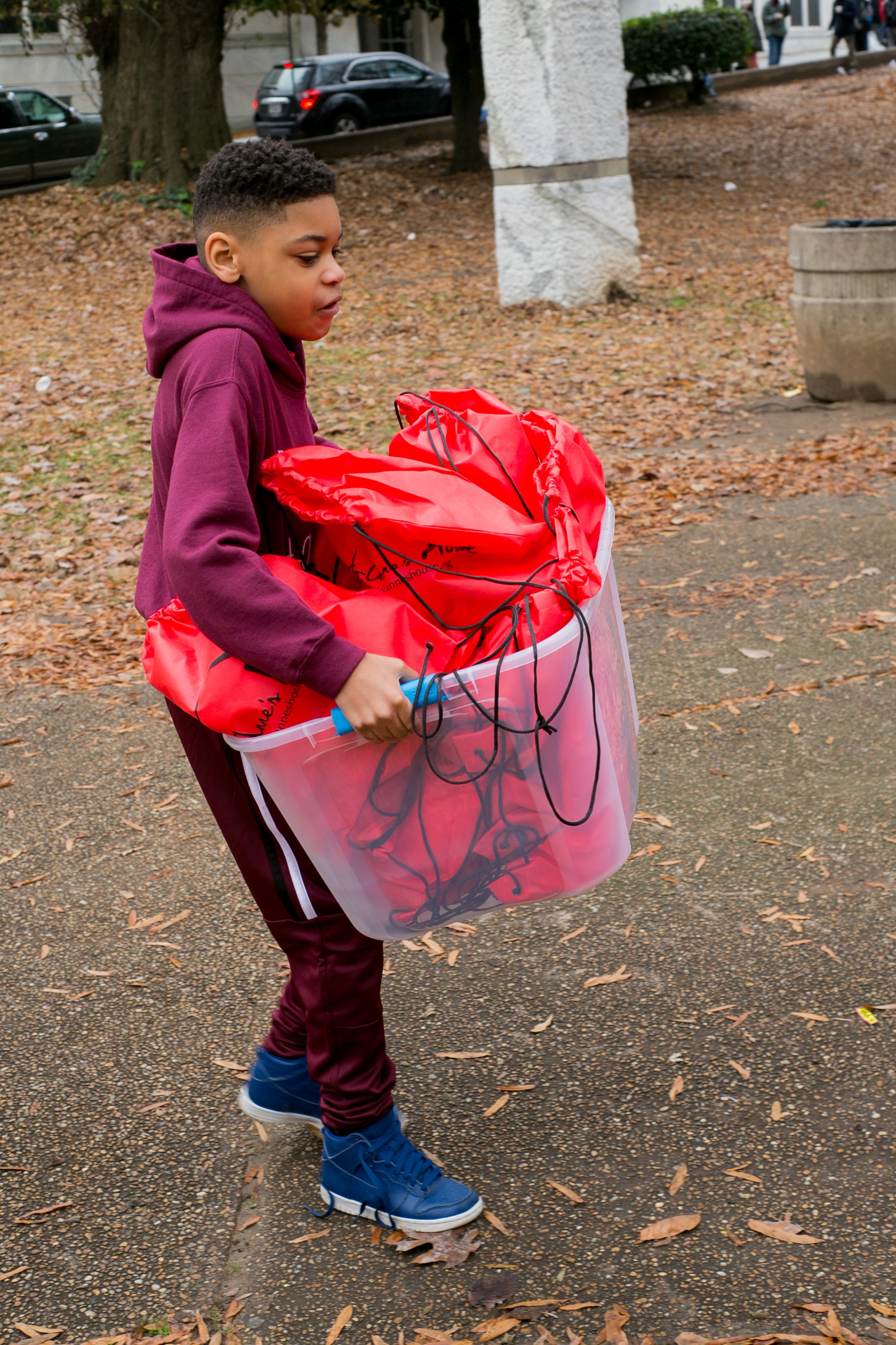 A young volunteer carrying a bin full of red care bags across the park