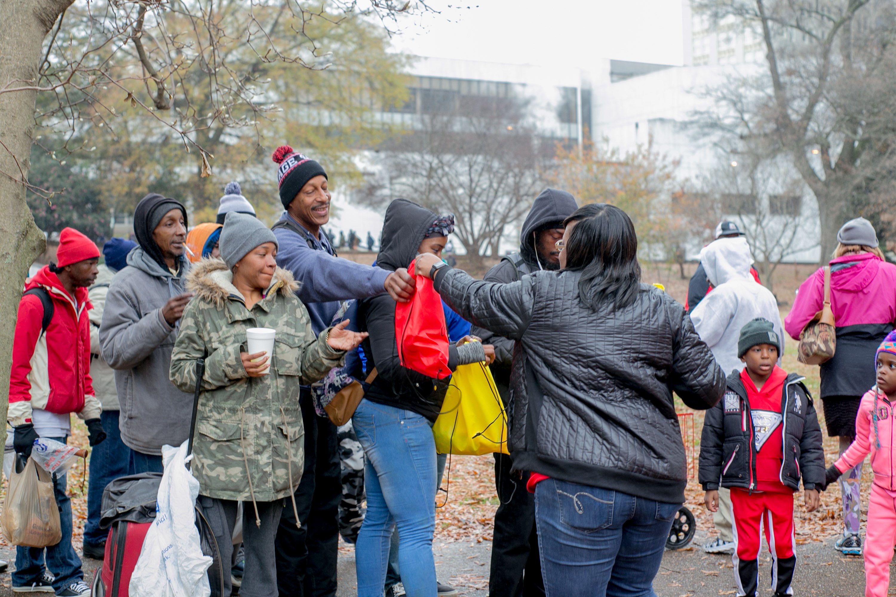 A volunteer handing red and yellow care bags to people gathered at the outreach