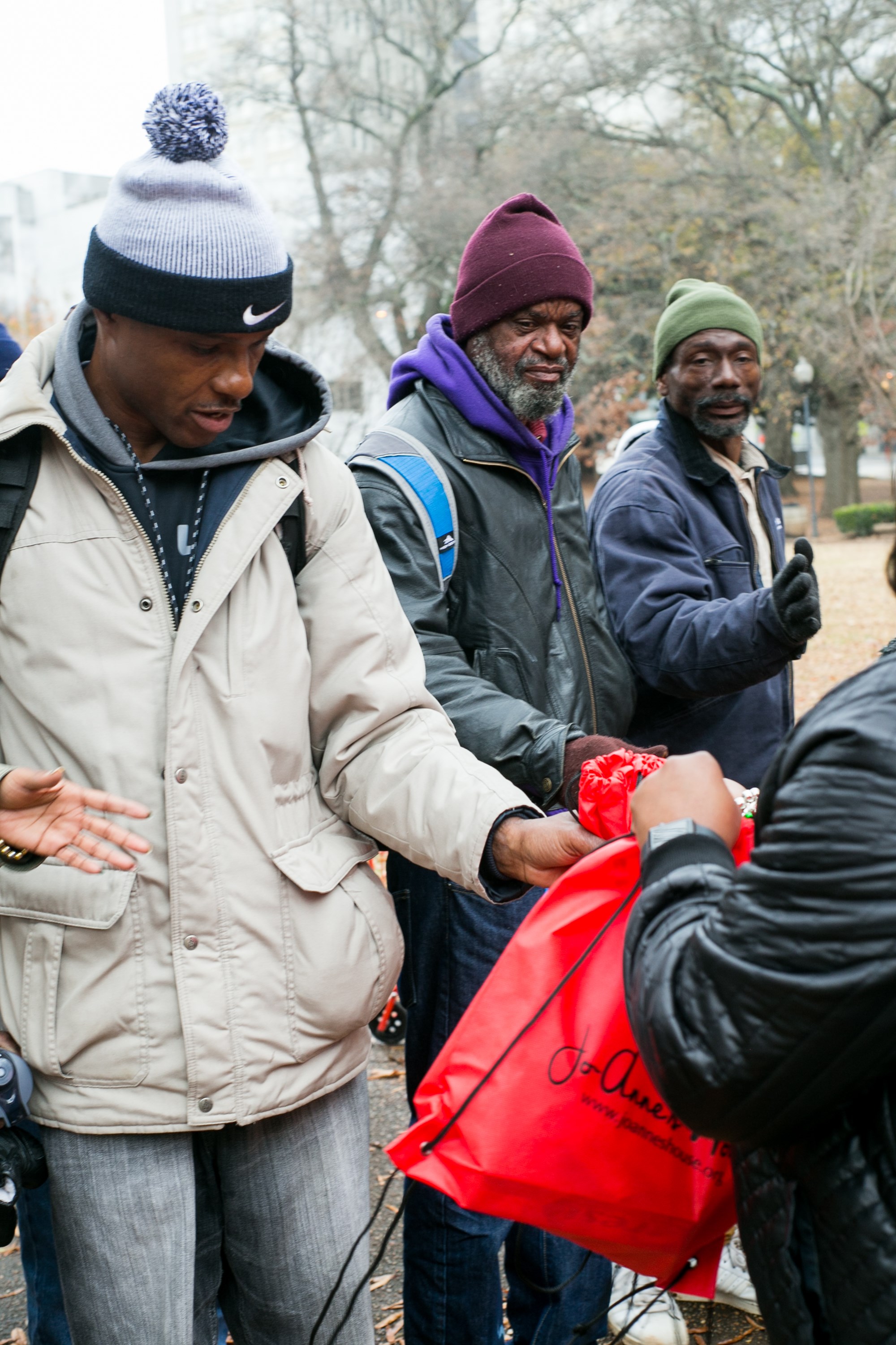 A volunteer handing a red Jo-Anne's House care bag to a group of men in winter coats