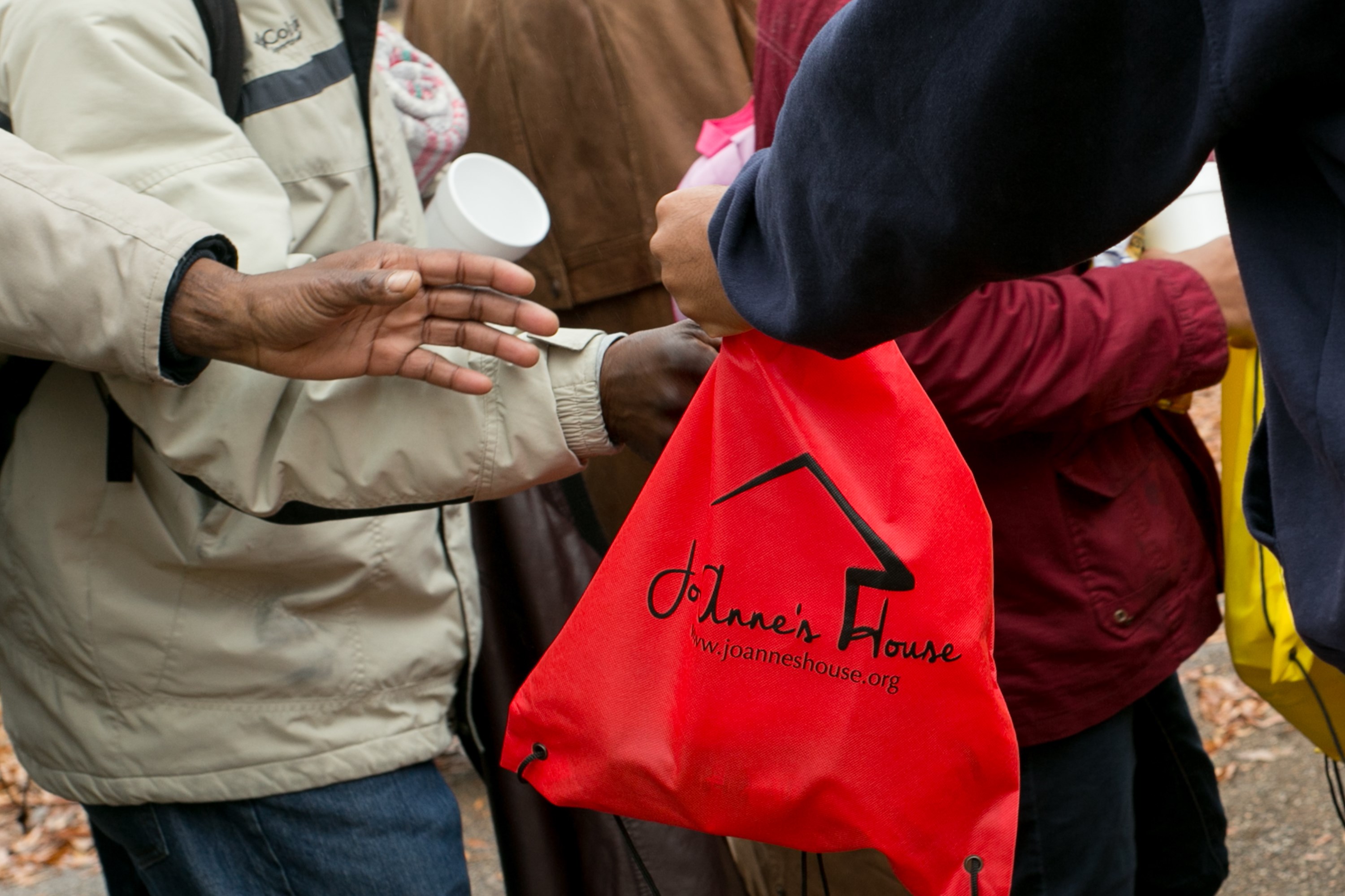 Close-up of a red Jo-Anne's House drawstring care bag being handed to a recipient