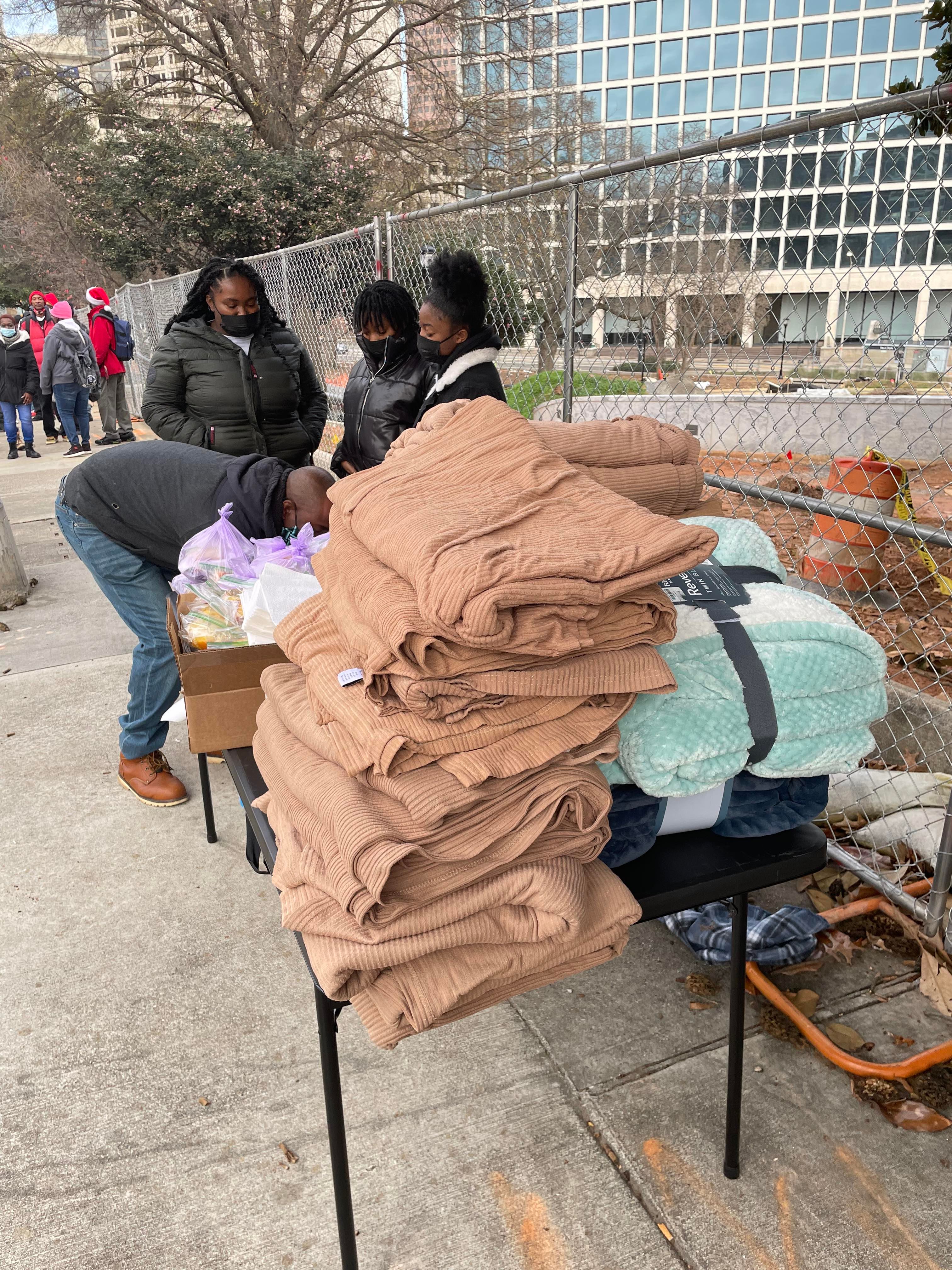 Volunteers behind a table stacked with folded blankets and meal bags