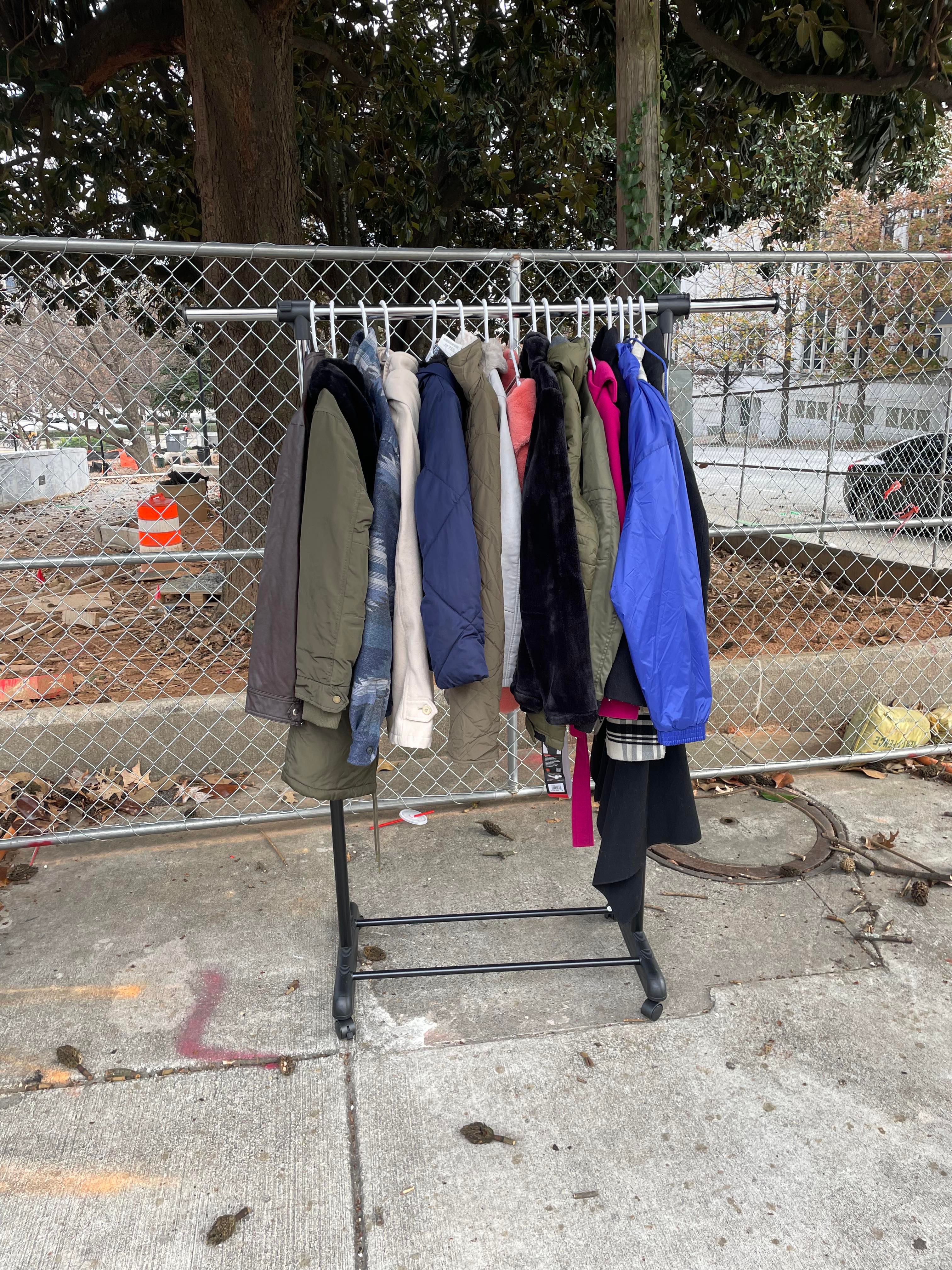 A rolling rack of donated winter coats along a fence at the outreach site