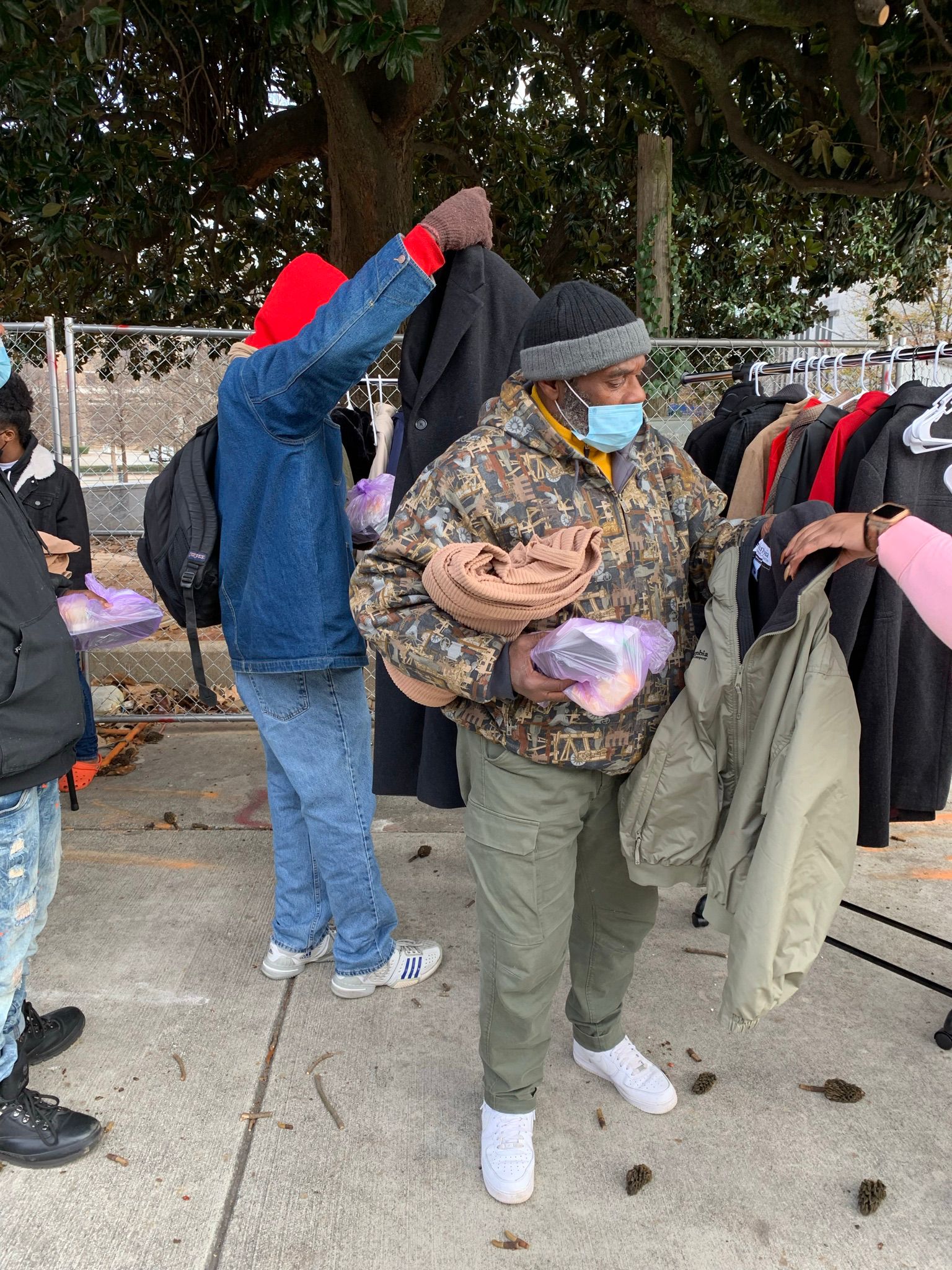 A man selecting a coat from a rack while holding a meal bag and blanket