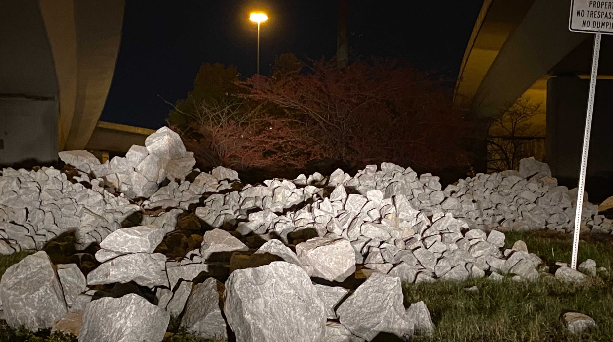 White boulders under a bridge at night beside a "No Trespassing, No Dumping" sign