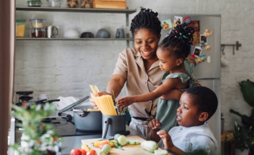 A mother cooking a meal in the kitchen with her two young children