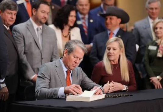 Georgia Governor Brian Kemp signs legislation at a table surrounded by state officials