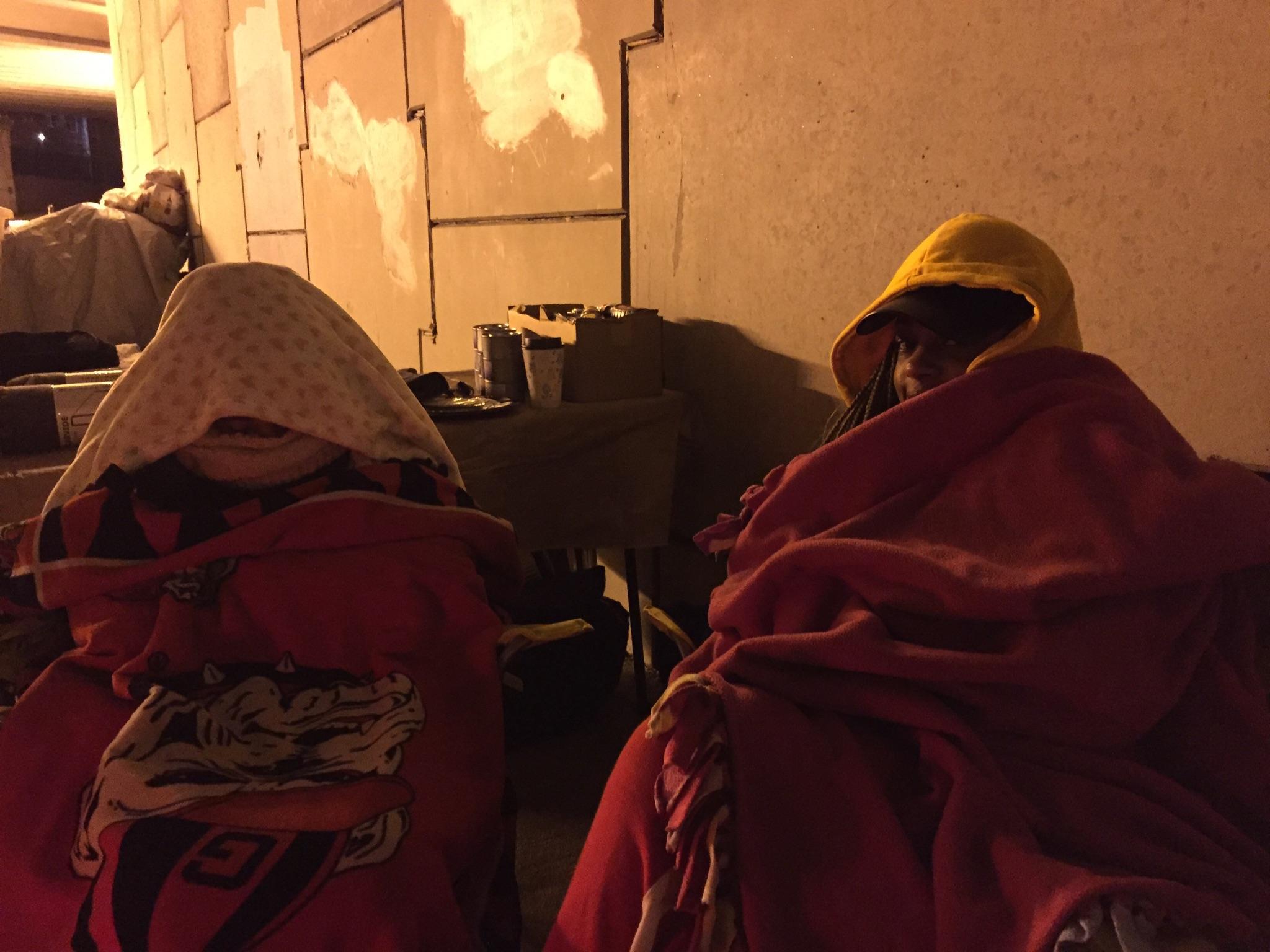 Two people bundled in blankets and hoods staying warm through the night