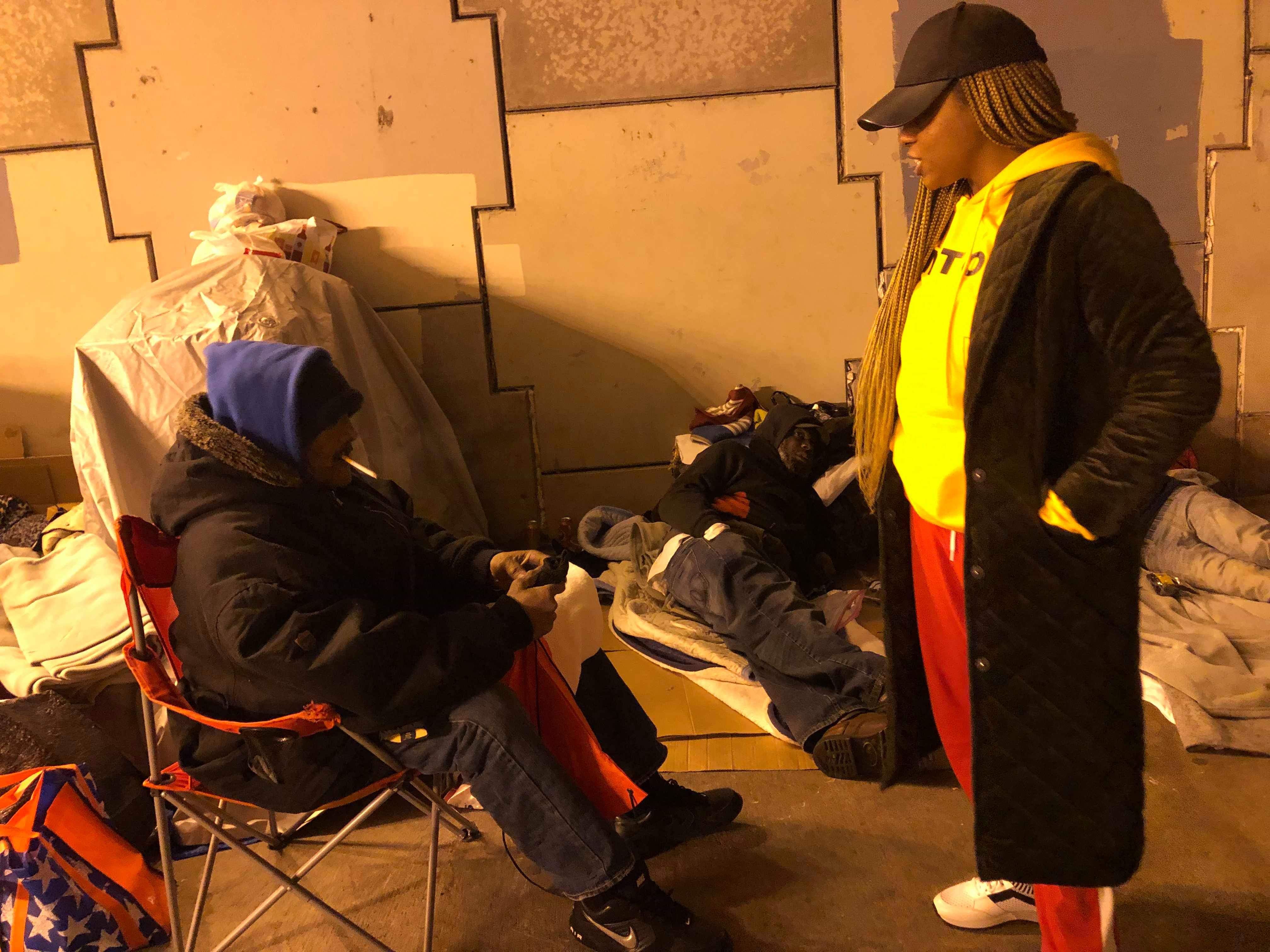 A volunteer in a yellow hoodie speaking with residents sitting and reclining under the bridge