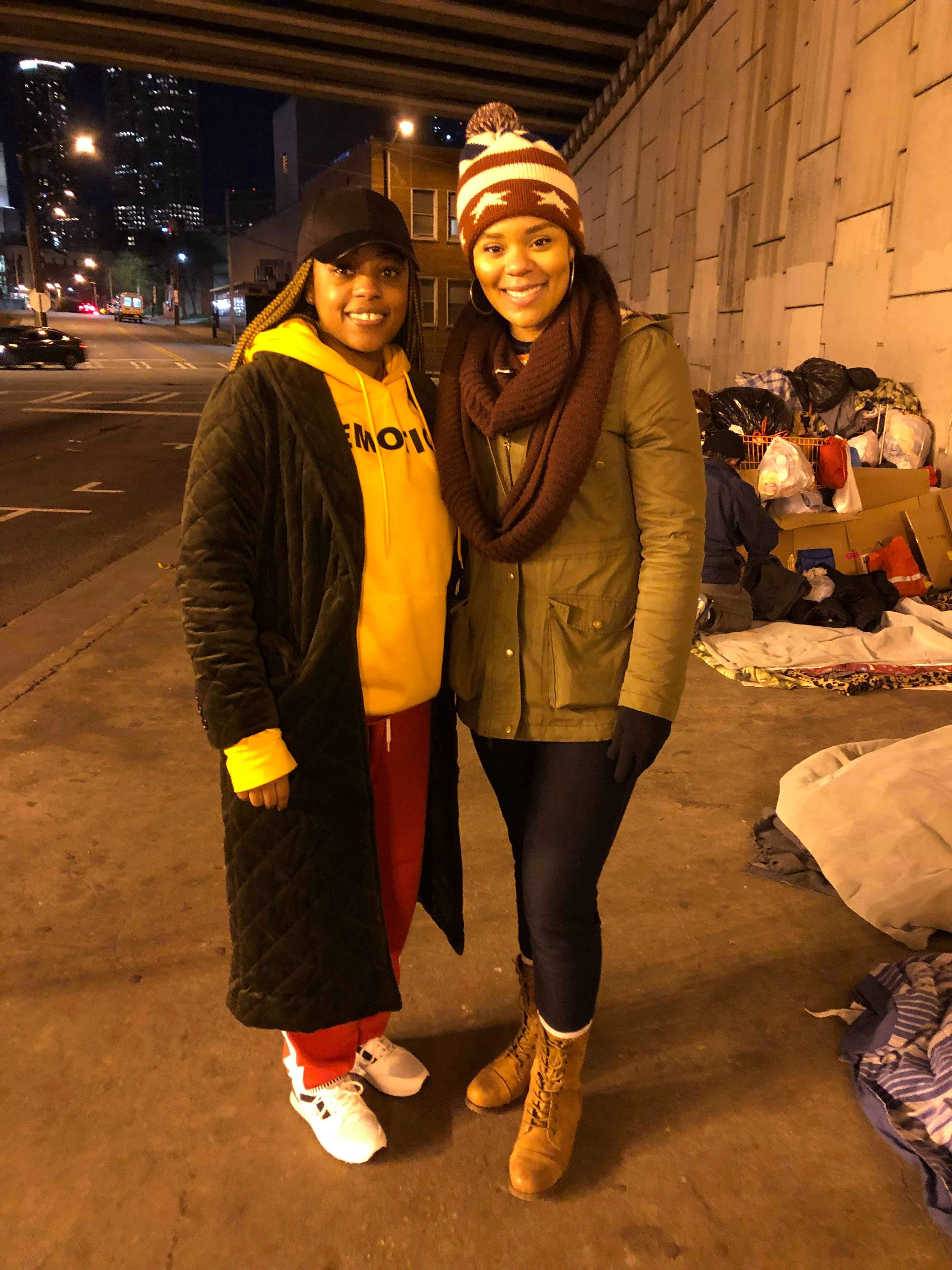 Two volunteers standing together beside the encampment under the bridge