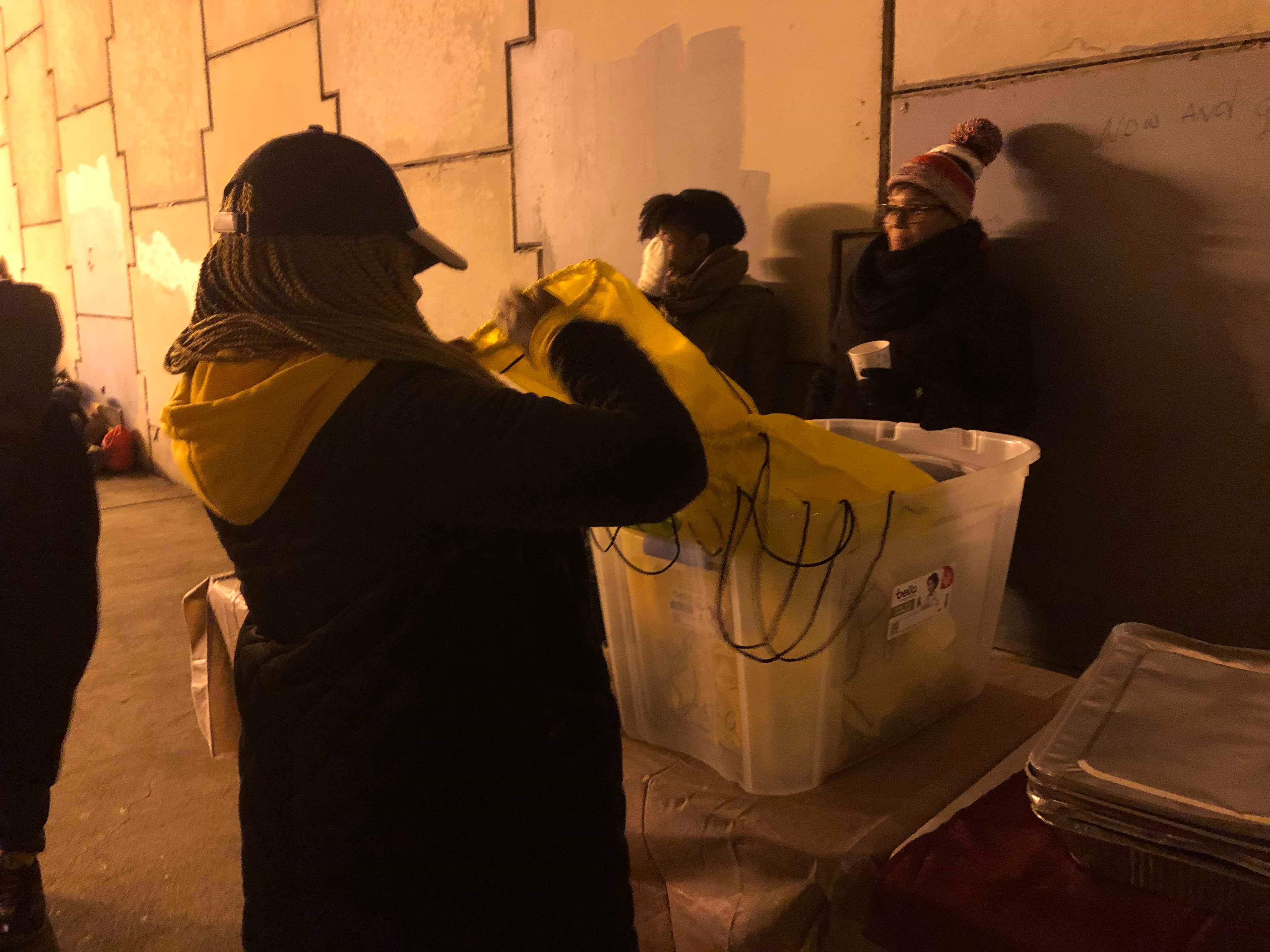 A volunteer handing out a poncho from a supply bin to those gathered