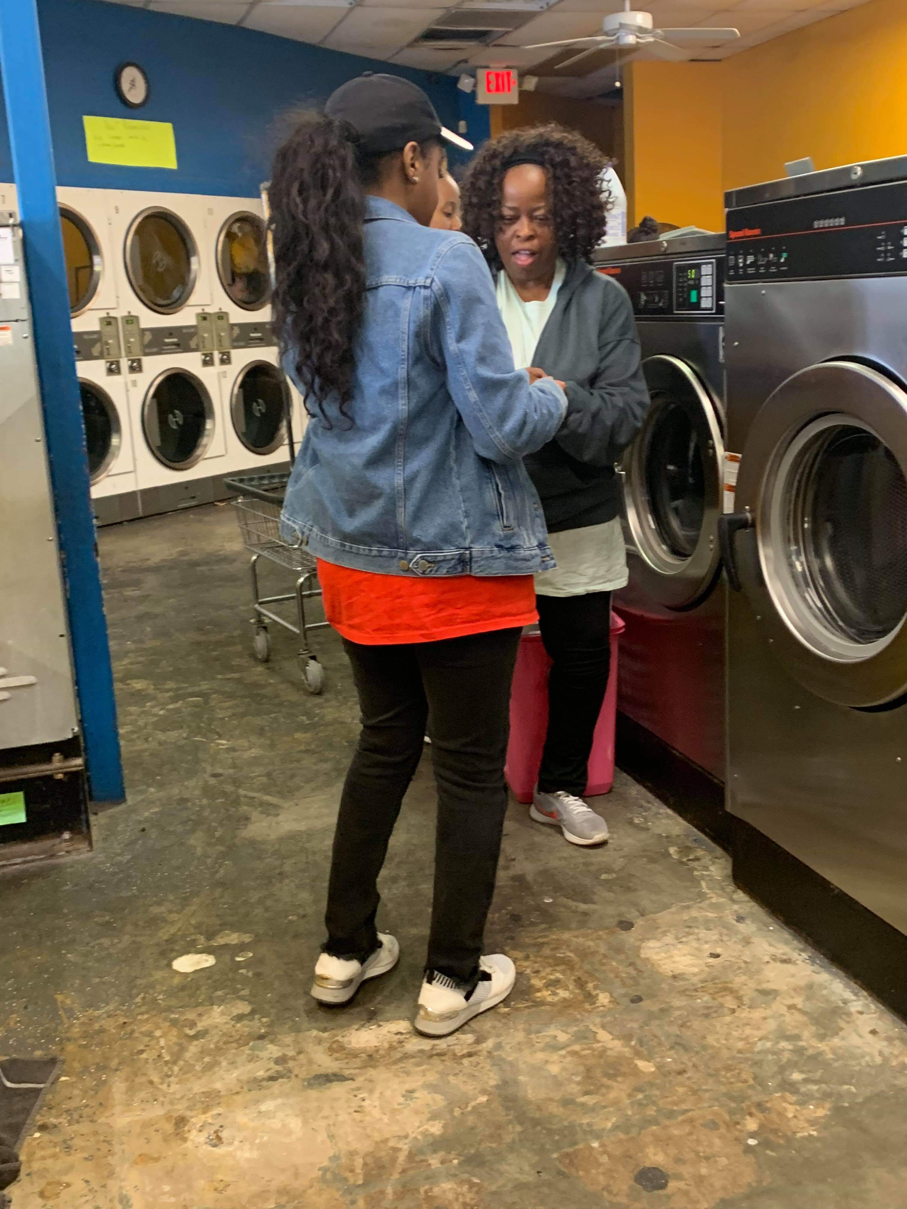 A Jo-Anne's House volunteer talking with a community member beside the washing machines