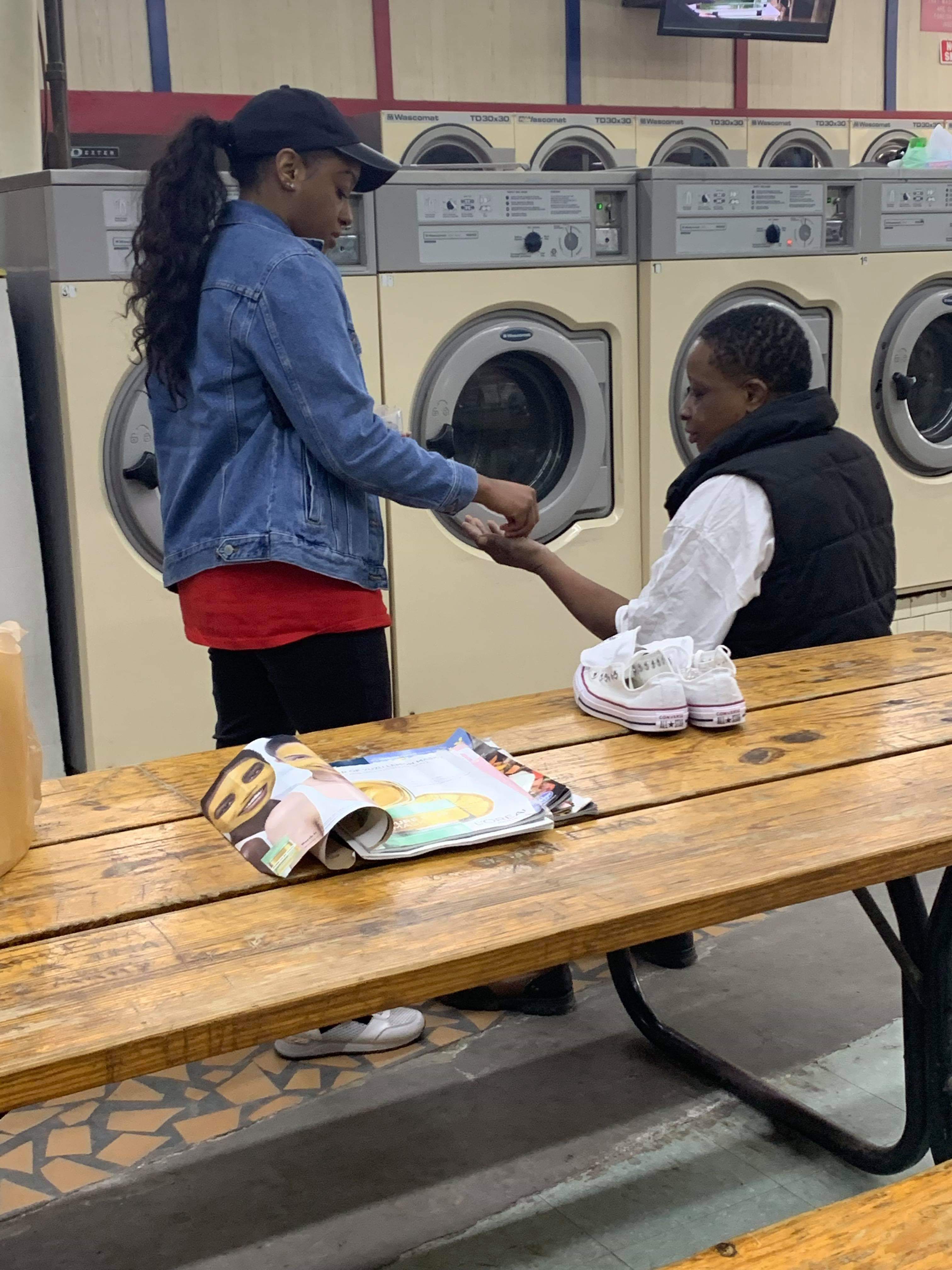 A volunteer holding a pop-up laundry hamper while chatting with a smiling laundromat patron
