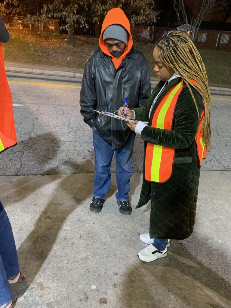 A volunteer with long braids writing on a clipboard while interviewing a man at night