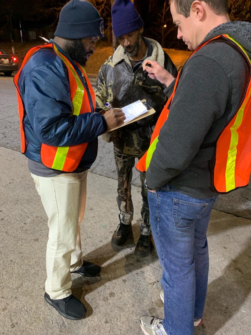 Two volunteers in orange safety vests surveying a man at night during the count