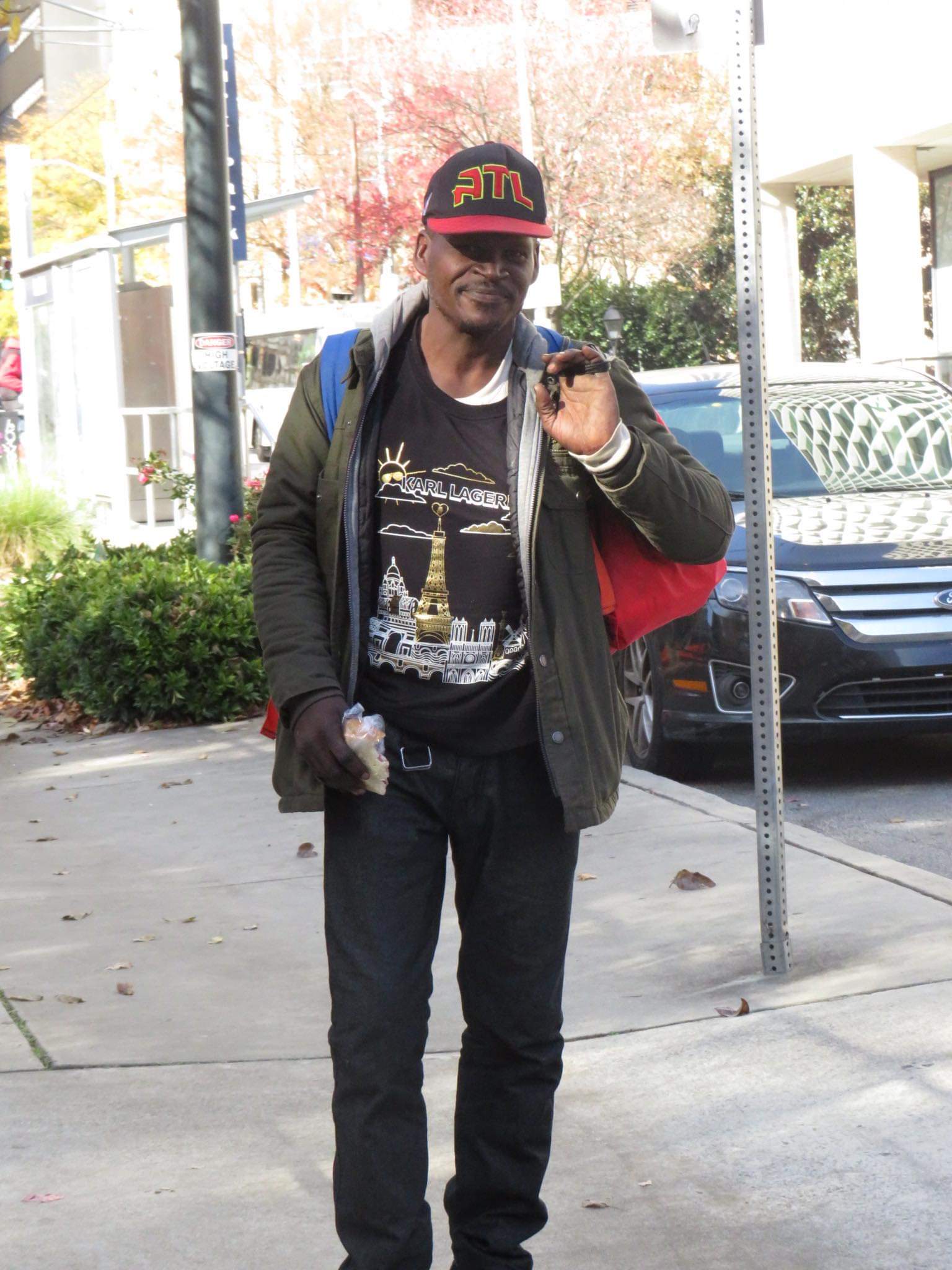 A smiling man in an ATL cap holding food and carrying a red Jo-Anne's House care bag